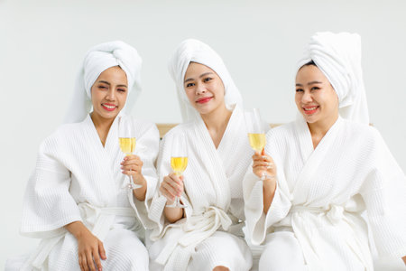 Millennial three Asian female customers friends in white clean bathrobes and towels have appointment...