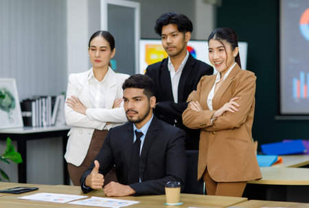 Millennial Asian Indian professional successful bearded businessman entrepreneur ceo sitting taking photo with male female employees staffs officers in formal business suit stand crossed arms behind.の写真素材
