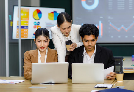 Millennial Asian Indian professional multinational male businessmen and female businesswomen in formal business suit standing sitting in meeting room mentoring brainstorming together with laptop.の写真素材