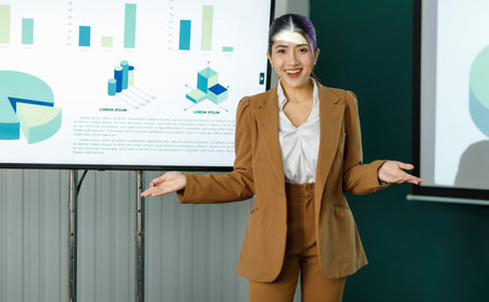 Millennial Asian happy professional successful female businesswoman presenter trainer standing presenting business ideas strategy graphs charts on monitor in meeting room.の写真素材