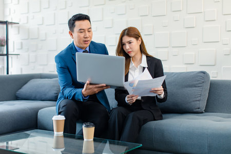 Asian professional successful male senior businessman mentor teaching helping explaining information in laptop computer to female intern businesswoman secretary in formal business suit in living room.の写真素材