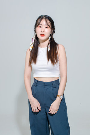 Portrait isolated cutout studio shot of Asian young pretty female fashion model with pigtails braids hairstyle in fashionable sleeveless crop top shirt cargo pants standing posing on white background.の写真素材