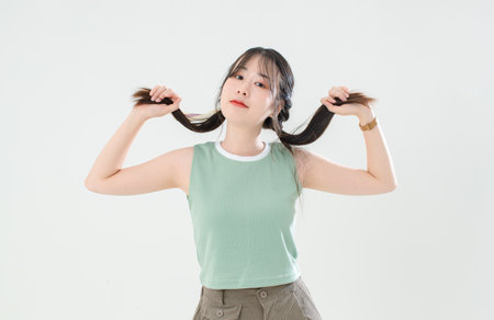 Portrait isolated cutout closeup studio shot of Asian young cute female teenage fashion model in casual trendy wear standing smiling posing holding hands on pigtails braids hair on white background.の写真素材