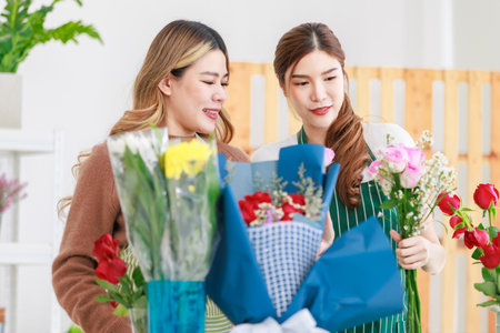 Asian professional successful female florist designer flower shop owner entrepreneur and colleague employee helping decorating flower bouquet in vase in floral garden store studio.の写真素材