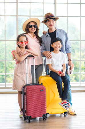 Asian cheerful happy family mom dad son and daughter wearing sunglasses and hat standing posing with two trolley luggages smiling celebrating holiday together ready for traveling vacation road trip.の写真素材