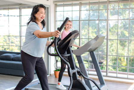 Asian happy healthy old chubby retirement pensioner mother smiling using elliptical machine exercise...