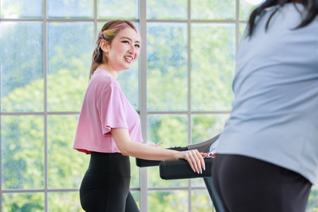 Asian happy healthy young beautiful daughter smiling using walking running on adjustable pad machine exercise working out with old retirement pensioner mother in living roomの写真素材