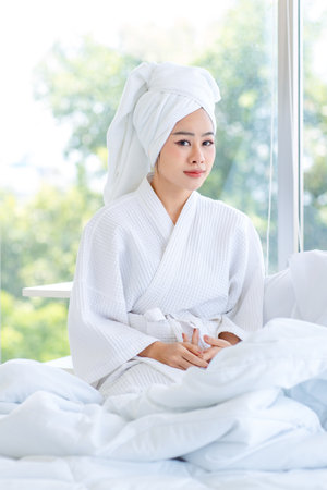 Asian young pretty sexy female teenager girl in bathrobe ready for relaxing spa on bed sitting smiling playing with cute little domestic orange long hair companion pet cat kitty in towel in bedroom.の写真素材