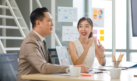 Asian professional successful male businessman manager mentor in formal business suit standing helping teaching supporting female businesswoman colleague sitting working with laptop notebook computer.の写真素材