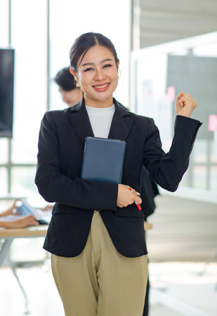 Asian professional successful female businesswoman entrepreneur manager ceo in formal business suit smiling standing posing crossed arms holding pen and touchscreen tablet computer in meeting room.の写真素材
