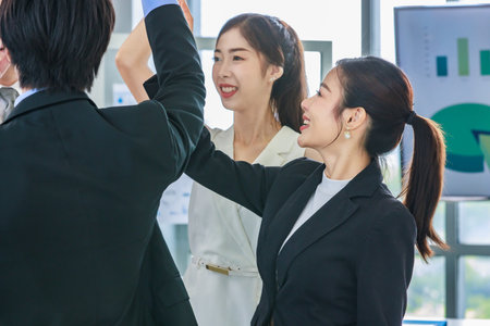 Group of Asian professional successful female businesswomen and male businessmen employee in formal business suit standing smiling holding hands high five together after job achievement deal done.の写真素材