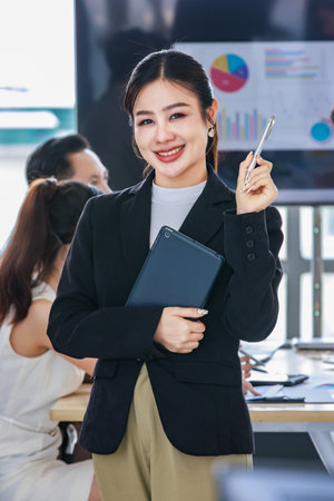 Asian professional successful female businesswoman entrepreneur manager ceo in formal business suit smiling standing posing crossed arms holding pen and touchscreen tablet computer in meeting room.の写真素材