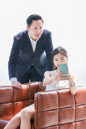 Asian professional successful female businesswoman secretary employee showing calling online mobile phone to male businessman manager in formal business suit in living roomの写真素材