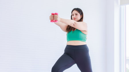 Asian young chubby fat healthy oversized overweight fit female sportswoman in sportswear sports bra legging standing stretching lifting dumbbells exercising training practicing in home fitness gym.の写真素材