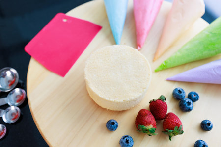 Top view closeup shot of delicious tasty homemade baking chiffon cake placed on wooden tray with colorful decorating piping whipping cream and mixed berries strawberry blackberry blueberry in kitchen.の写真素材