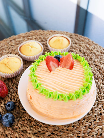 Top view closeup shot of delicious tasty yummy homemade baking strawberry fruit orange green sponge cake and cupcakes placed on wooden weave ratten tray decorating with organic fresh raw blackberry.の写真素材