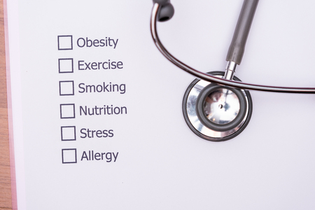 On the doctor's desk, Doctor assess the patient's history and what are the risks to cause a disease with his Diagnose Form.の写真素材