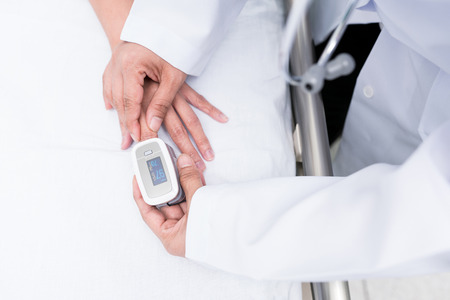 Doctor measuring blood oxygen levels of the sleeping elder patient on bed with oximeter.