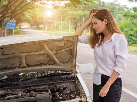 Young woman looking at broken down car on streetの写真素材