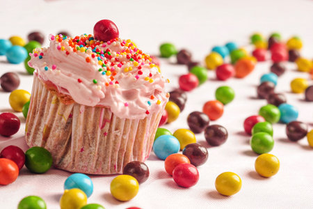 Cupcakes decorated with candy and colorful sprinkles with round candies scattered on the floorの写真素材