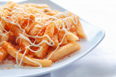 French fries decorated with mayonnaise and balado seasoning are placed on a white plate