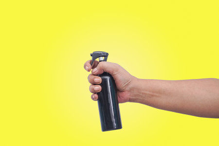 close up of hand hold a spray bottle. isolated on yellow backgroundの写真素材