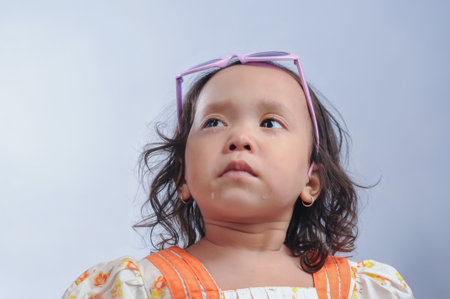 An Indonesian little girl after crying and wearing dress and glasses. isolated on plain backgroundの写真素材