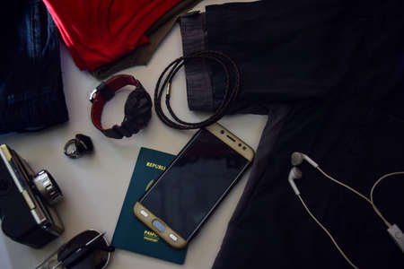 Passport, sunglasses, old camera, jeans, shirt, watches, bracelet and sunglasses are lying on white background. Preparing for travelingの写真素材