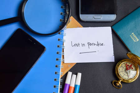 Travel Concept Inspiration - Lost in Paradise written on paper. passport, magnifying glass, Compass, Smartphone, book on black backgroundの写真素材