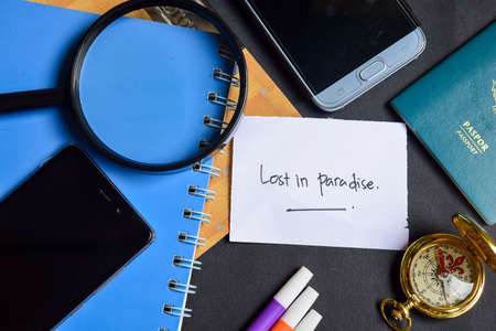 Travel Concept Inspiration - Lost in Paradise written on paper. passport, magnifying glass, Compass, Smartphone, book on black backgroundの写真素材