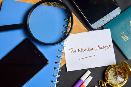 Travel Concept Inspiration - The Adventure Begins written on paper. passport, magnifying glass, Compass, Smartphone, book on black backgroundの写真素材