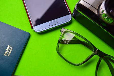 travel and vacation concept. passport, smartphone, eyeglass, analog camera isolated green backgroundの写真素材