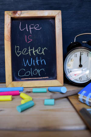 Life is better with color. Back to school concept. Alarm clock on wooden with blackboard on...