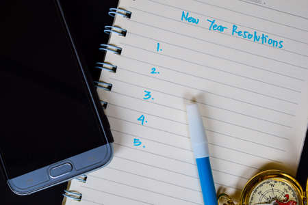 New year resolutions text on notebook, compass, color pencil, smartphone on black background, for...