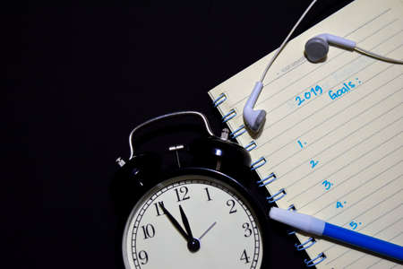 2019 Goals text on notebook, alarm clock, color pen, earphone on black background, for business presentation mock up for adding your listの写真素材