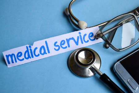 Conceptual image with Medical service inscription with the view of stethoscope, eyeglasses and smartphone on the blue background. Medical Conceptual.の写真素材