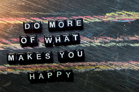 Do More of What Makes You Happy on wooden blocks. Cross processed image with blackboard background. Inspiration, education and motivation conceptsの写真素材
