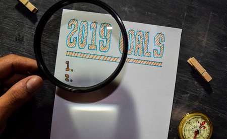2019 Goals handwritten text on the paper with marker, compass and use magnifying glass on blackboard...