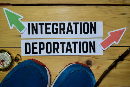 Integration or Deportation opposite direction signs with sneakers, eyeglasses and compass on wooden vintage background. Business, education and finance conceptsの写真素材