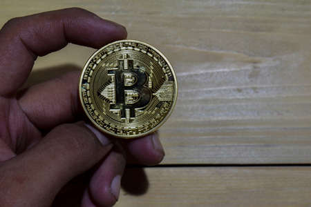 Bitcoin gold in man hand on wooden table background. When throwing up with a finger conceptの写真素材