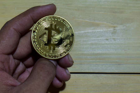 Bitcoin gold in man hand on wooden table background. When throwing up with a finger concept