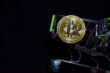 Bitcoin gold and shopping cart on black background. Bitcoin outside a shopping cart. Business...