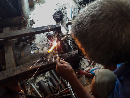 Editorial use only; blurred An old welder in a blue T-shirt use sunglasses. Rusty iron welding on...