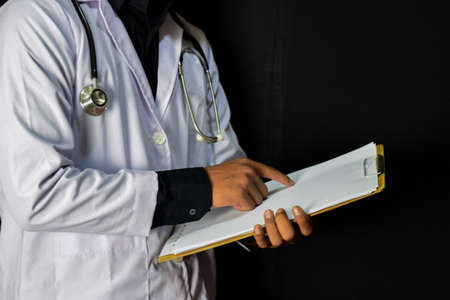 A doctor standing holding clipboard on black background. Medical and healthcare conceptの写真素材