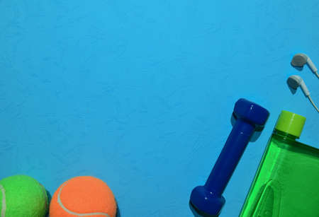 Blue dumbbell, Green tennis ball, earphone and bottle indicating workout plan on blue background....