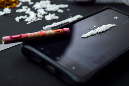 Cocaine, Indonesia rupiah and smartphone ready for uses on dark table. Selective focus on cocaineの写真素材