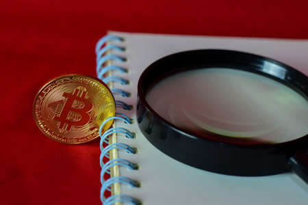 Coin bitcoin, notebook and a magnifying glass isolated on red background, extraction of crypto...