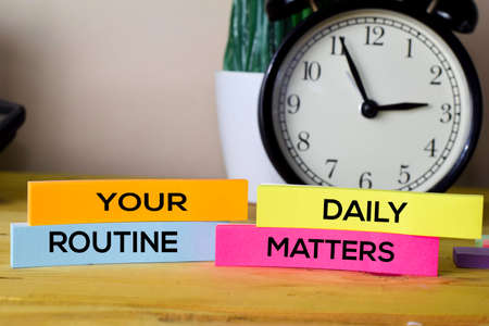 Your Daily Routine Matters. Handwriting on sticky notes in clothes pegs on wooden office deskの写真素材