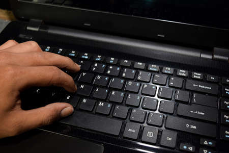 Hacker typing code on laptop keyboard with his fingersの写真素材