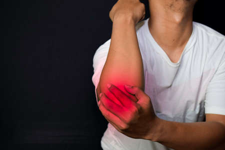 Asian Man Holding his hand. He feels pain on his elbow with black background. Medical or healthcare conceptの写真素材